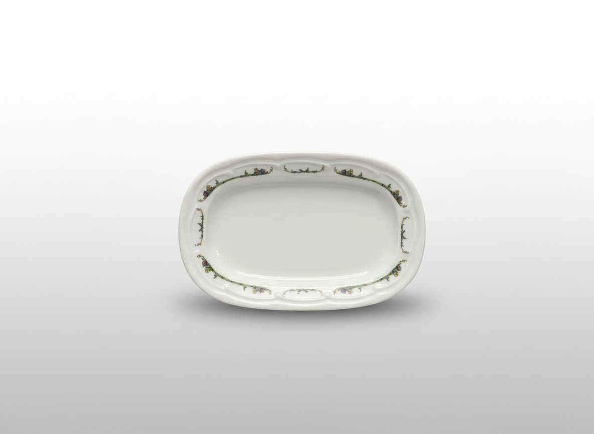 Iš viršaus nufotografuota balta stačiakampė dekoruota lėkštė 14 x 9,5 cm su gėlių ornamentais ant banguoto krašto.