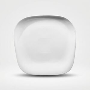 Išskirtinio dizaino balta kvadratinė lėkštė su užapvalintais kampais, stovinti ant balto paviršiaus.
