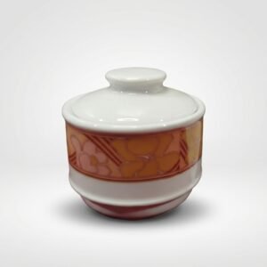 Baltas keraminis indelis su dangteliu, papuoštas oranžinių ir rausvų atspalvių gėlių raštu, stovintis ant balto paviršiaus.