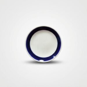 Iš viršaus nufotografuota maža balta lėkštutė su mėlynu kraštu, esanti ant šviesaus pagrindo.