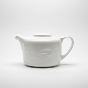Balta, arbatinuko formos, 400 ml keraminė pieninė su dangteliu ir reljefiniu raštu, nufotografuota ant balto fono iš šono.