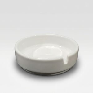 Ant balto fono stovinti apvali, klasikinio dizaino balta keraminė peleninė su viena įpjova cigaretei pasidėti.