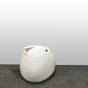 Ant tamsaus paviršiaus stovinti blizgi balta keramikinė cukrinė 300 ml su dangteliu ir išpjova šaukšteliui.